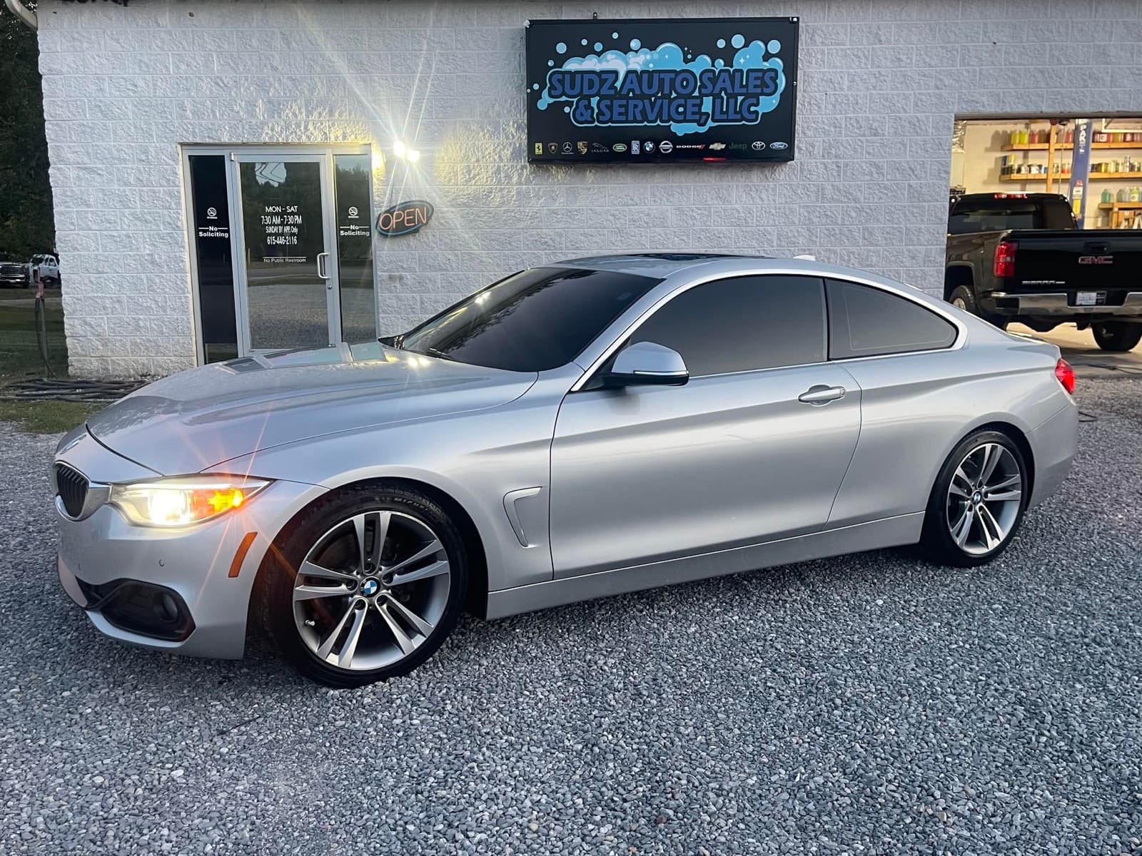 A detailed silver BMW coupe parked in front of the Sudz Auto Sales & Service storefront in Dickson, Tennessee